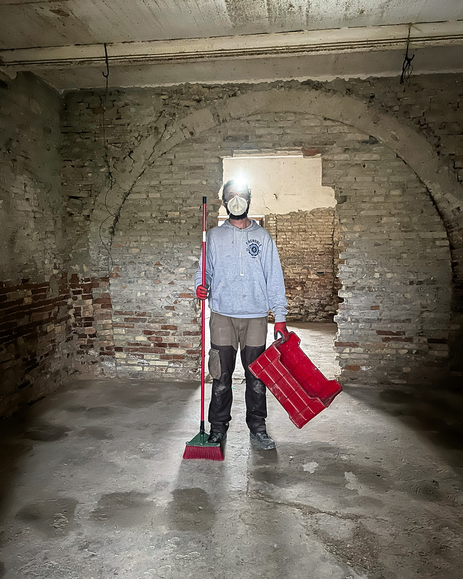 Person with headlamp holding a broom in empty room